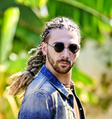 Çekici, sarışın, sakallı, erkek model, vahşi doğada saç örgüleri ve rastalı pozları var. Tarz, trendler, moda konsepti.