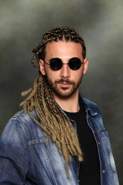 Attractive blonde male model with combination of braids and dreadlocks posing in studio on isolated background. Style, trends, fashion concept.