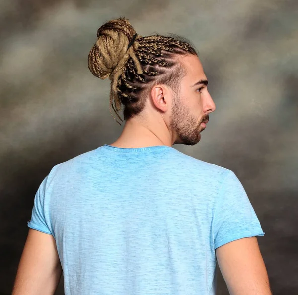 Attractive blonde male model with combination of braids and dreadlocks posing in studio on isolated background. Style, trends, fashion concept.