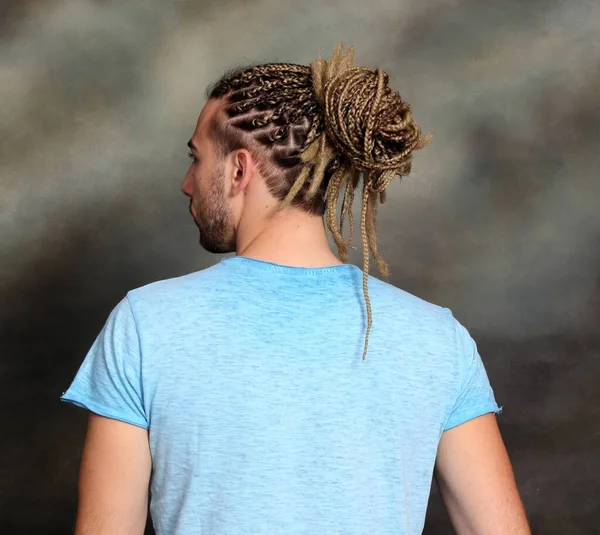 Attractive blonde male model with combination of braids and dreadlocks posing in studio on isolated background. Style, trends, fashion concept.