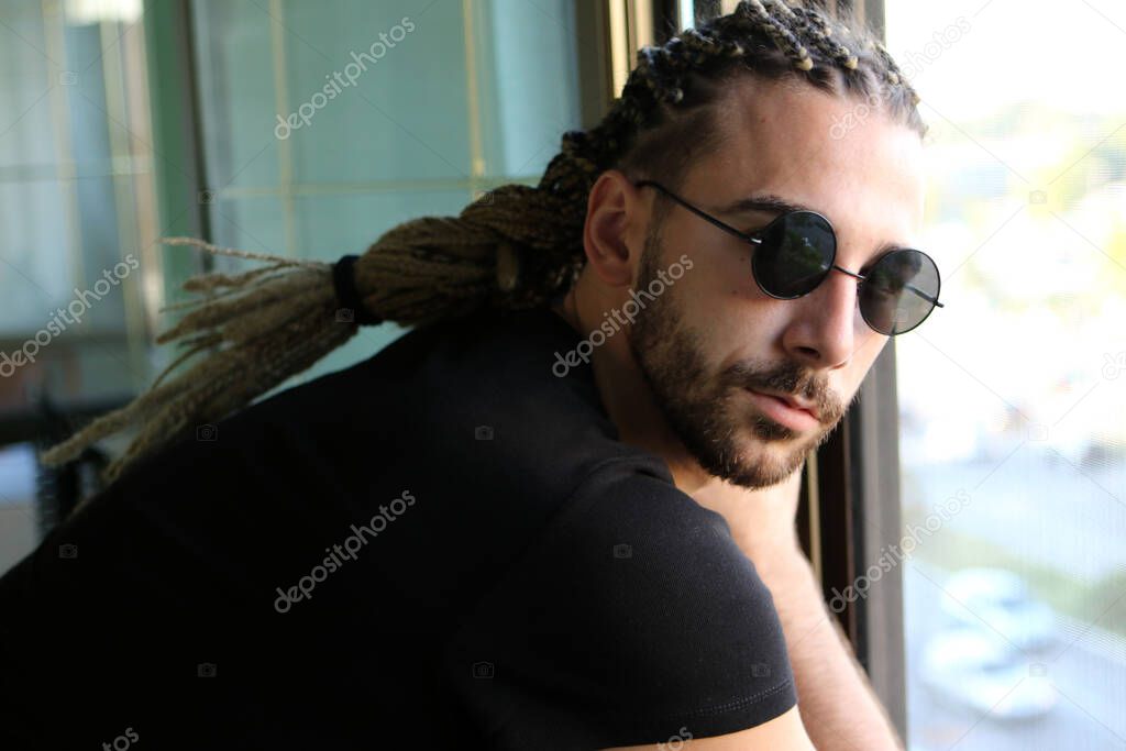 Attractive, young blonde bearded male model with combination of braids and dreadlocks posing on the balcony. Style, trends, fashion concept