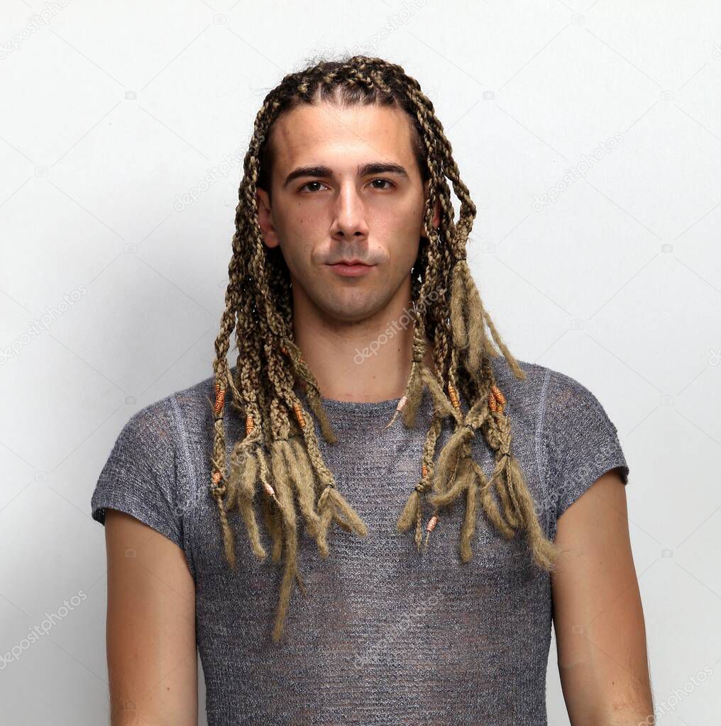 Attractive blonde male model with combination of braids and dreadlocks posing in studio on isolated background. Style, trends, fashion concept.