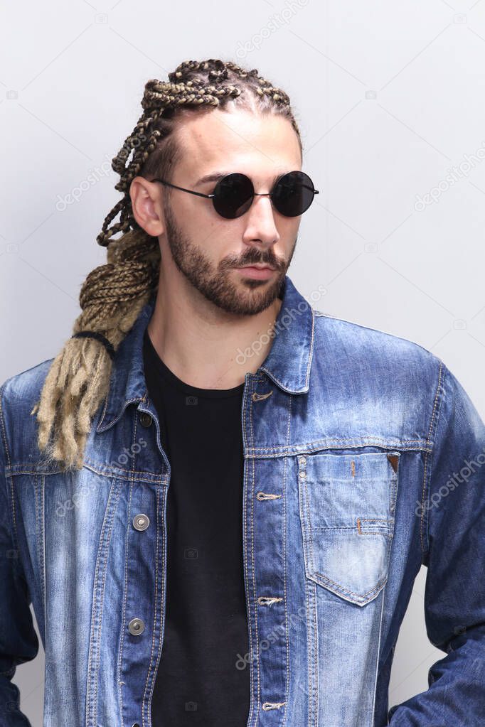 Attractive blonde male model with combination of braids and dreadlocks posing in studio on isolated background. Style, trends, fashion concept.