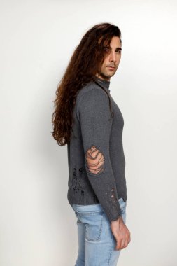 Uzun kıvırcık saçlı çekici genç adam stüdyoda poz veriyor. Tarz, trendler, moda konsepti.