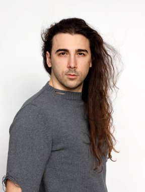 Uzun kıvırcık saçlı çekici genç adam stüdyoda poz veriyor. Tarz, trendler, moda konsepti.