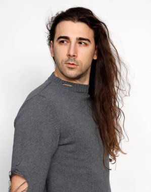 Uzun kıvırcık saçlı çekici genç adam stüdyoda poz veriyor. Tarz, trendler, moda konsepti.