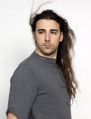 Uzun kıvırcık saçlı çekici genç adam stüdyoda poz veriyor. Tarz, trendler, moda konsepti.