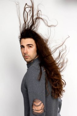 Uzun kıvırcık saçlı çekici genç adam stüdyoda poz veriyor. Tarz, trendler, moda konsepti.