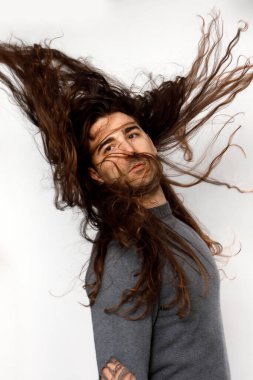 Uzun kıvırcık saçlı çekici genç adam stüdyoda poz veriyor. Tarz, trendler, moda konsepti.