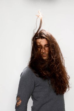 Uzun kıvırcık saçlı çekici genç adam stüdyoda poz veriyor. Tarz, trendler, moda konsepti.