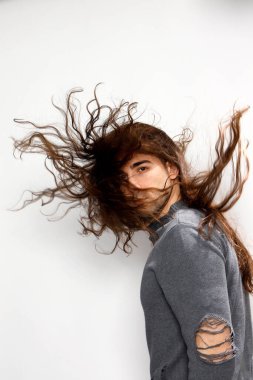 Uzun kıvırcık saçlı çekici genç adam stüdyoda poz veriyor. Tarz, trendler, moda konsepti.