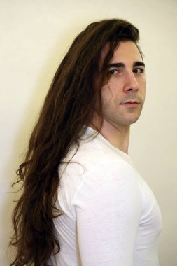 Uzun kıvırcık saçlı çekici genç adam stüdyoda poz veriyor. Tarz, trendler, moda konsepti.