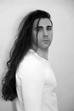 Uzun kıvırcık saçlı çekici genç adam stüdyoda poz veriyor. Tarz, trendler, moda konsepti.