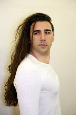 Uzun kıvırcık saçlı çekici genç adam stüdyoda poz veriyor. Tarz, trendler, moda konsepti.