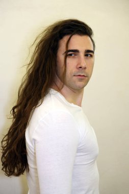 Uzun kıvırcık saçlı çekici genç adam stüdyoda poz veriyor. Tarz, trendler, moda konsepti.