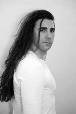 Uzun kıvırcık saçlı çekici genç adam stüdyoda poz veriyor. Tarz, trendler, moda konsepti.