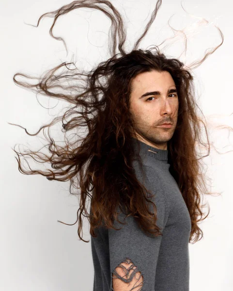 Attractive young guy with very long curly hair is posing in studio. Style, trends, fashion concept.