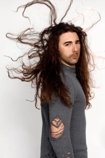 Attractive young guy with very long curly hair is posing in studio. Style, trends, fashion concept.