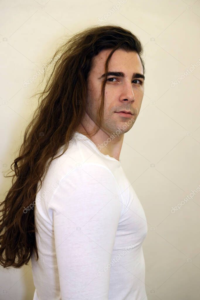 Attractive young guy with very long curly hair is posing in studio. Style, trends, fashion concept.