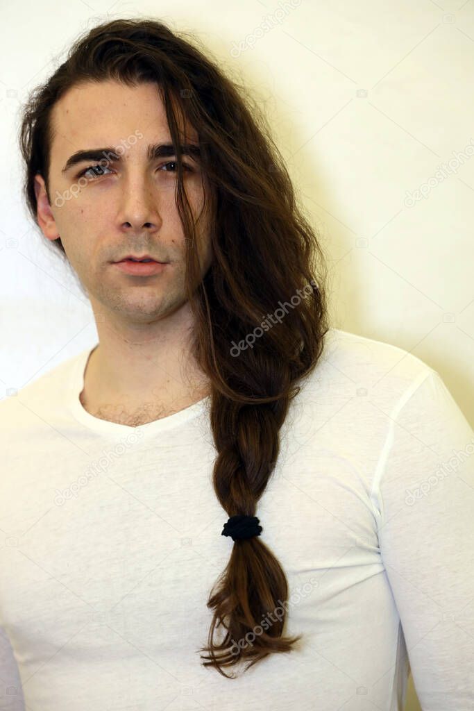 Attractive young guy with plaits is posing indoors. Style, trends, fashion concept.