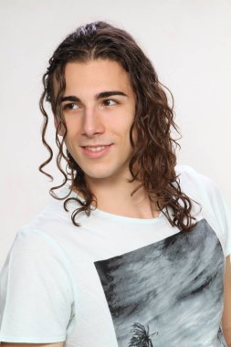 Uzun kıvırcık saçlı çekici genç adam stüdyoda poz veriyor. Tarz, trendler, moda konsepti.