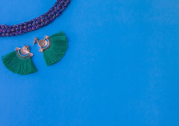 green earrings and purple necklace on blue background