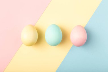 Pastel paskalya yumurtaları geometrik arkaplanda mavi, sarı ve pembe renkte. Modern konsept.