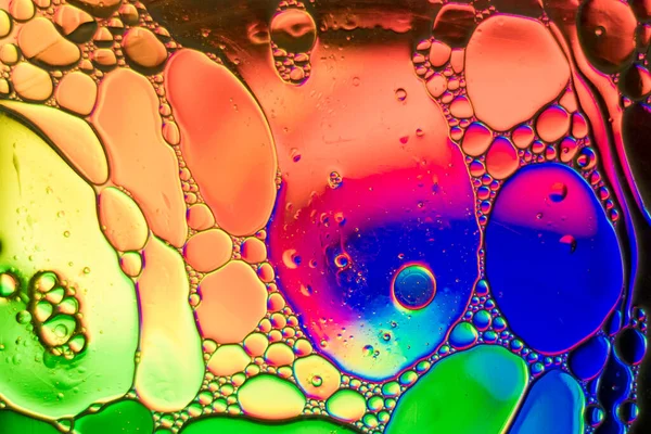 Photography with an abstract theme, with drops of oil mixing with water inside a glass container that is on top of a tablet with psychedelic drawings.
