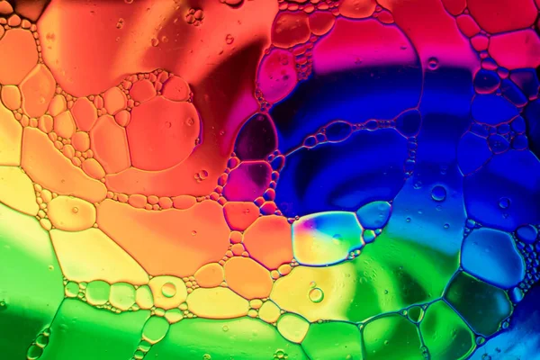 Photography with an abstract theme, with drops of oil mixing with water inside a glass container that is on top of a tablet with psychedelic drawings.