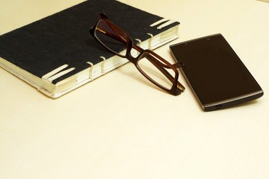 Gözlük, siyah defter ve ahşap arka plan üzerinde akıllı telefon.