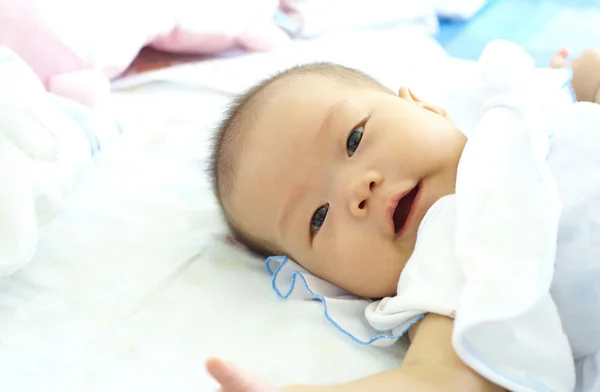 Bambina sdraiata sul letto. Carino bambino in abito bianco è sorridente — Foto Stock