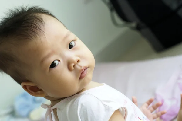 Asian infant sit on the pink bed and looking for something. — Stock Photo, Image