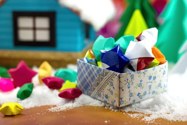 Paper stars in a gift box on the snow, with the small house and