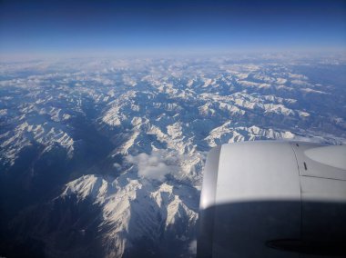 Mavi gökyüzü, beyaz bulutlar ve uçak penceresinde dağlar