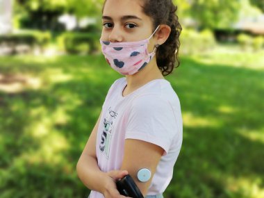Corona virus  and diabetes. Girl with the mask on face checks glucose level in blood with device for continuous glucose monitoring  CGM before entering school. Insulin depend. Diabetes type 1 clipart