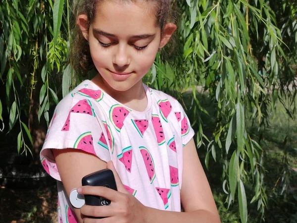 Girl with diabetes checks glucose level in blood with device for continuous glucose monitoring  CGM. She is reading glucose level from the white sensor on right arm. Insulin depend. Diabetes type 1.