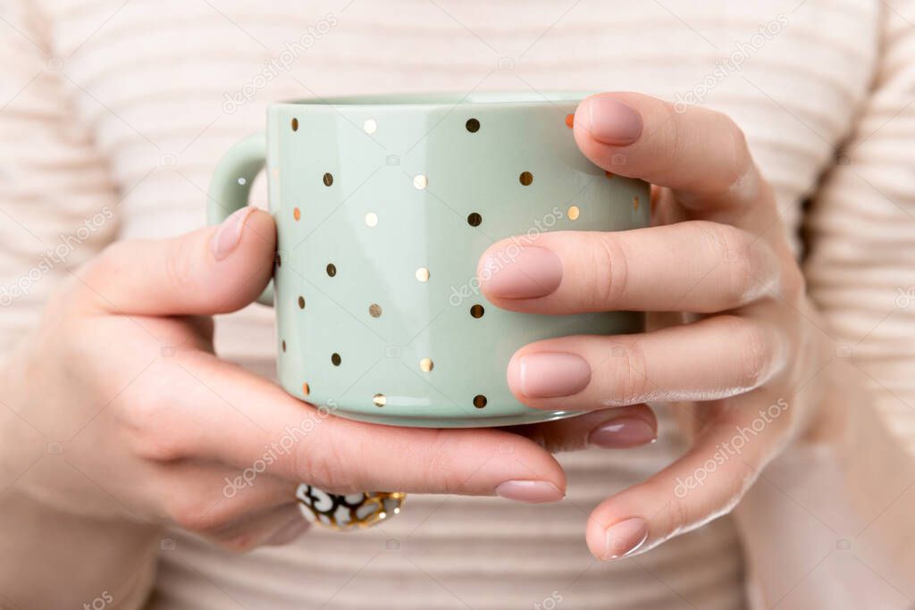 Woman with groomed hands with nude beige pink nail design holding cup