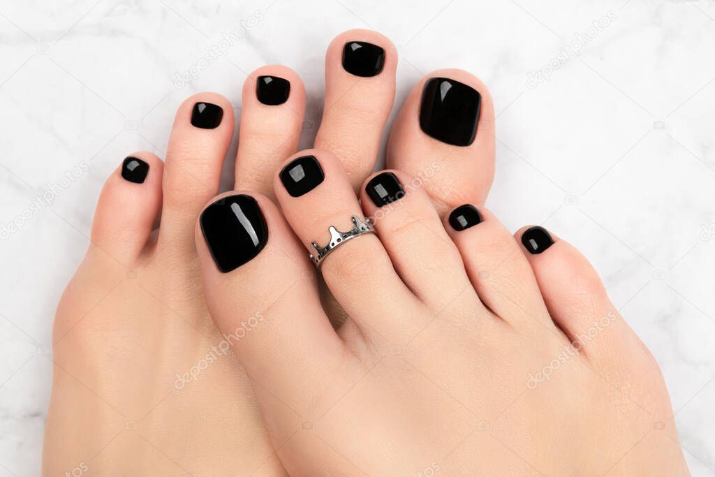 Womans feet on marble background. Beautiful classic black nail design