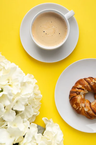 White cup of coffee and flowers on yellow background. Flat lay top view breakfast concept