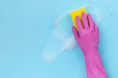 Kadınlar ellerini pembe lastik eldivenlerle yıkarlar mavi arka planda süngerle.
