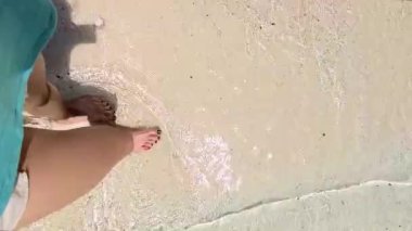 Plajda yürüyen yeşil tırnak tasarımlı kadın bacakları.