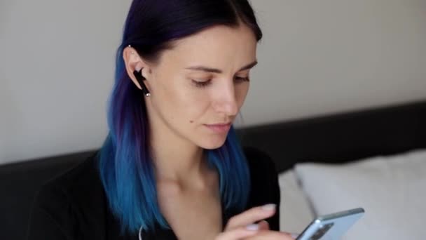Mulheres hipster Pensivas com fones de ouvido sem fio no quarto trabalham com smartphone — Vídeo de Stock