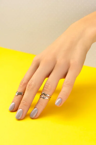 Hermosa mano de las mujeres con diseño de uñas brillantes sobre fondo gris y amarillo —  Fotos de Stock