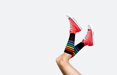 Şık kırmızı spor ayakkabılı kadın bacakları ve gri arka planda gökkuşağı çorapları.