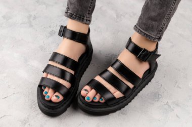 Gri arka planda siyah sandaletli pedikürlü kadın ayakları