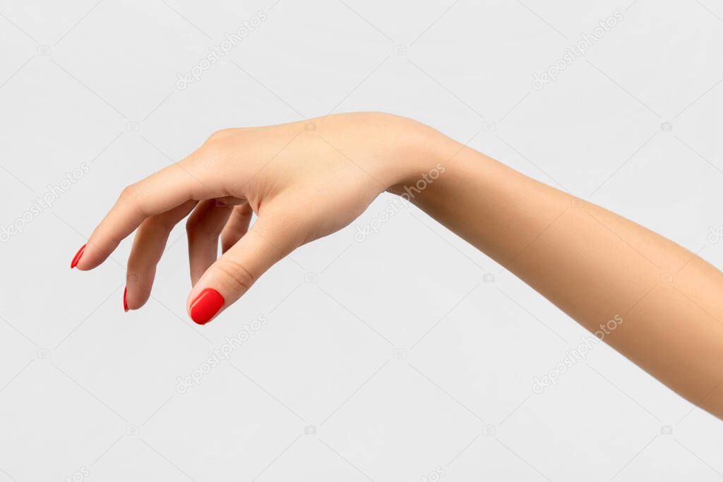 Beautiful young womans hand with red manicure on gray background