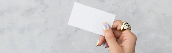 Manicured womans hand holding postcard on grey concrete background