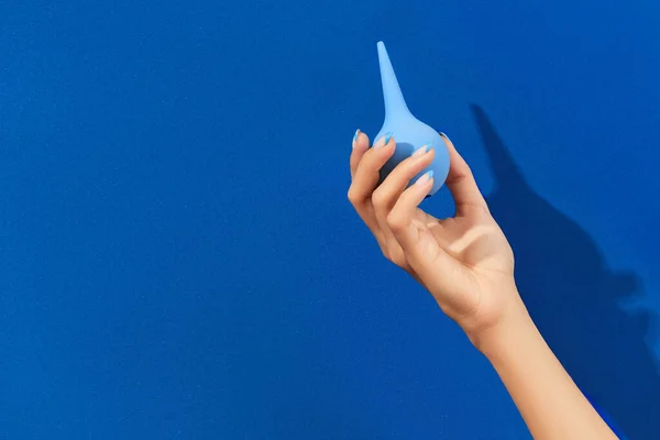 Dobře upravené ženy ruka drží klystýr na modrém pozadí — Stock fotografie