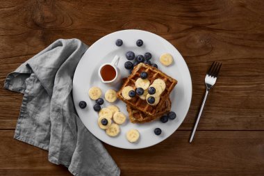 Kırsal ahşap masada muzlu ve yaban mersinli Belçika waffle 'ı. Sağlıklı kahvaltı diyet tarifi