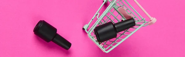 Botellas planas vista superior de esmalte de uñas en el carrito de la compra sobre fondo rosa vibrante — Foto de Stock